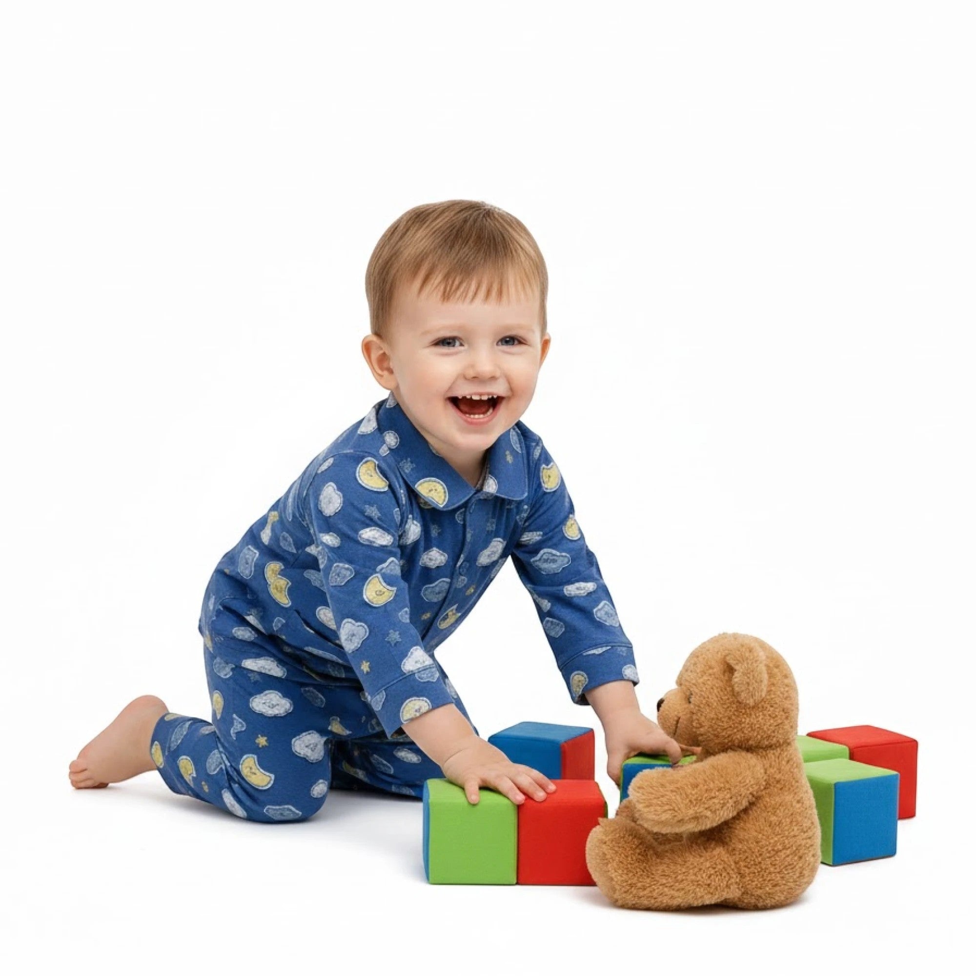 Lilloom blue cotton pajama set with moons, clouds, and stars print. A happy toddler plays with blocks and a teddy bear.