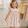 Young girl in a floral dress standing in a room with clothing racks.