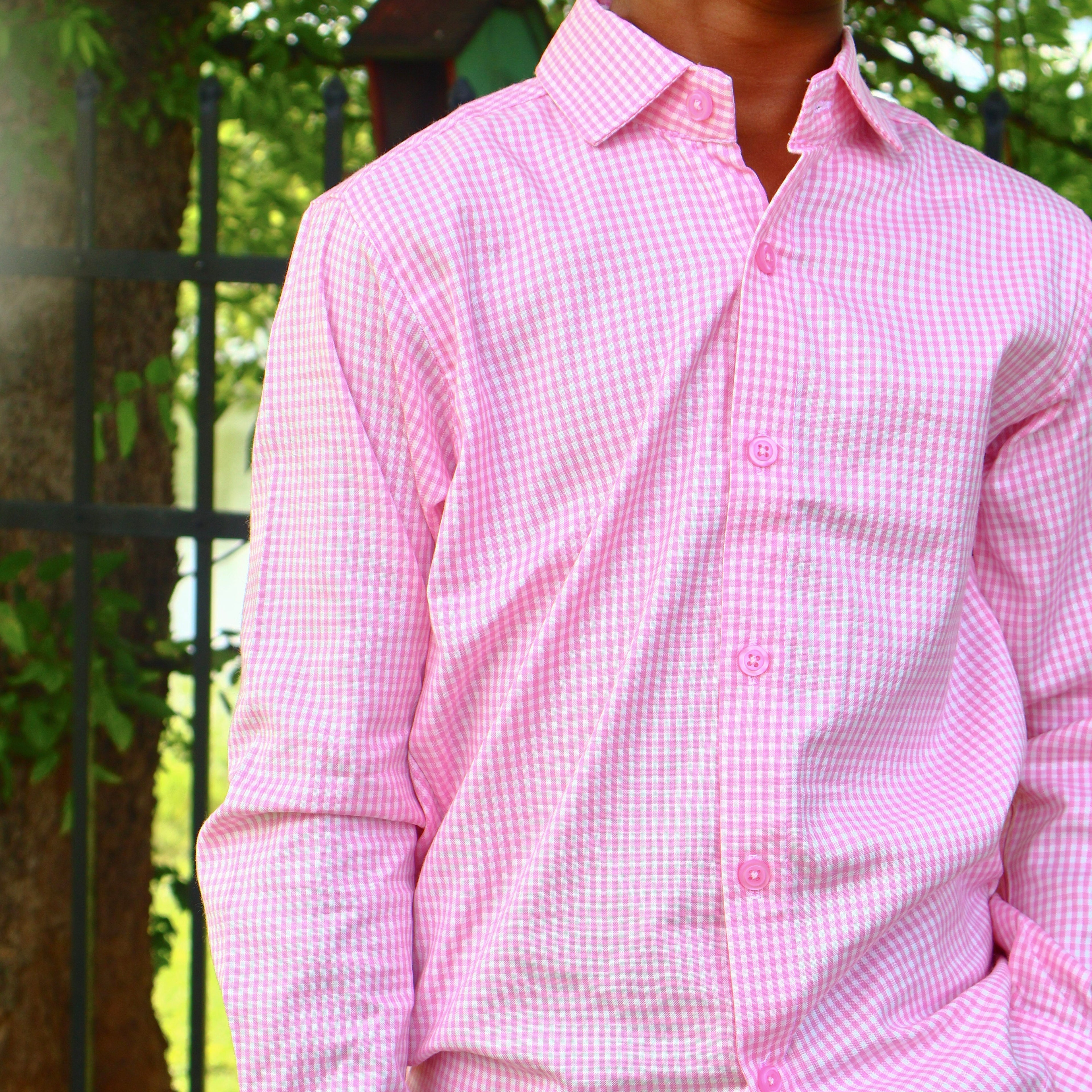Person wearing a pink checkered shirt outdoors with greenery in the background